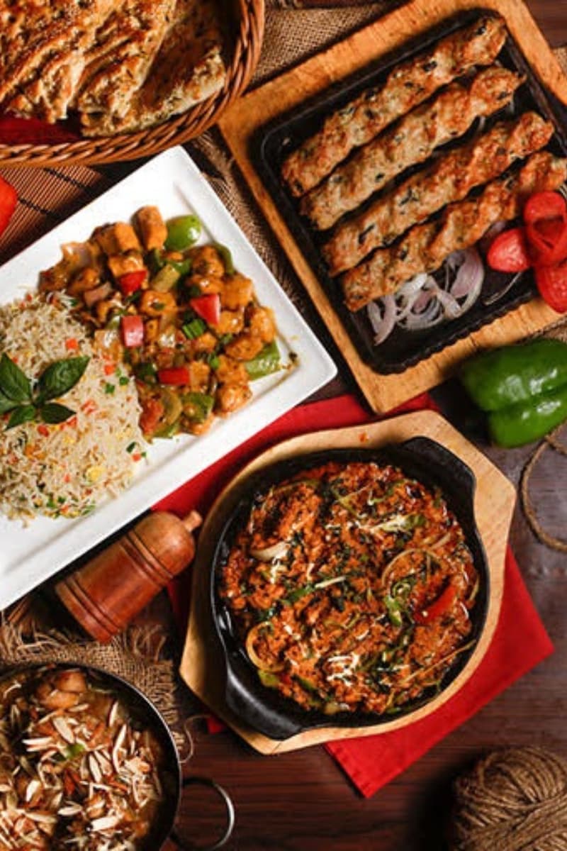 Feast spread with biryani, kebabs, curries, and naan on a white table